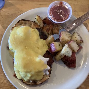 Sunrise Grill - Irish eggs Benedict - A breakfast plate featuring Irish eggs Benedict topped with melted cheese, roasted potatoes, and a small cup of ketchup, served on a white plate. - American Near Me - Kittery, Maine