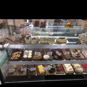 The Sweet Mustache - a display case full of cakes and pastries - A bakery display case showcases an assortment of cakes, cookies, and pastries, each labeled with handwritten tags, with some items on wooden trays. - Desserts Near Me - Eagle, Colorado