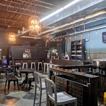 Brew Practitioners - The interior of Brew practitioners. - The photo depicts the interior of Brew Practitioners, a craft brewery featuring a mix of seating options including tables and chairs, a bar area with barstools, and decorative lighting fixtures hanging from the ceiling. The space has an industrial design with exposed ductwork and a tiled floor, creating a cozy yet modern atmosphere. - Breweries Near Me - East Longmeadow, Massachusetts