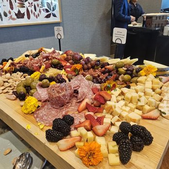 Conroux - Board - A large cheese and charcuterie board features assorted cheeses, grapes, strawberries, blackberries, nuts, and edible flowers on a wooden table. - Diners Near Me - Conroe, Texas