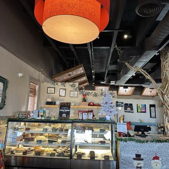 Range Cafe - The image shows the interior of a cafe decorated for the holiday season, including a white Christmas tree with ornaments, a large orange ceiling light, and festive decorations such as a snowman figure and garlands. A glass display case contains various baked goods, and the counter area has holiday-themed decor. The ceiling has exposed ductwork and skylights, with a person visible in the background. - Breakfast & Brunch Near Me - Albuquerque, New Mexico