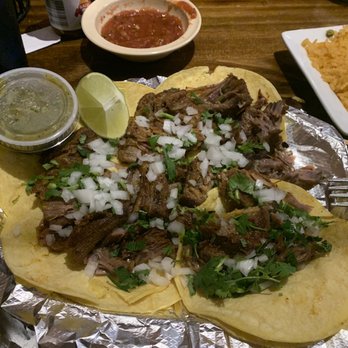 Las Fuentes - a plate of mexican food - Plate of tacos with shredded beef, chopped onions, and cilantro, accompanied by lime wedge, salsa, and side dishes including rice and sauce. - Mexican Near Me - Arnold, Missouri