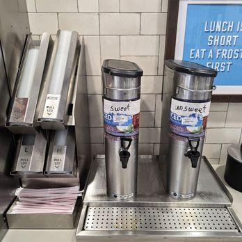 Wendy's - Two stainless steel beverage dispensers labeled 'sweet' and 'unsweet' are on a counter at Wendy's, with a sign in the background advising to eat a frosty first. - Burgers Near Me - Boonville, Missouri