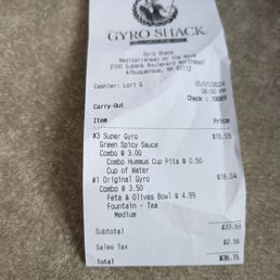 These prices we were charged were more than the menu said it would be. (My wife caught it and went up to complain and got $5 back.) - A crumpled paper receipt from Gyro Shack, located at 2100 Eubank Boulevard Northeast, Albuquerque, NM, is shown on a textured surface. It details a takeout order including a super gyro with green spicy sauce, combo hummus cup pita, and water, along with an original gyro, feta and olives bowl, and tea. The receipt includes the cashier's name, date, time, and total cost of $36.15, with tax and subtotal information.