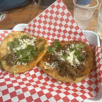 Chalmers - Fry bread tacos - Two fry bread tacos with meat, cheese, and cilantro are served on red and white checkered paper in a basket at a restaurant. - Bars Near Me - Austin, Texas