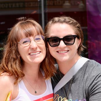The Larson Lens - Two people smiling with a pride flag in the background. - Videographers Near Me The Larson Lens - Two people smiling with a pride flag in the background. - Videographers Near Me