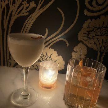 Silk Road - Two beverages (an old fashioned and the petro yuan) on a counter. A candle burns softly. - Cocktail Bars Near Me - Portland, Oregon Silk Road - Two beverages (an old fashioned and the petro yuan) on a counter. A candle burns softly. - Cocktail Bars Near Me - Portland, Oregon