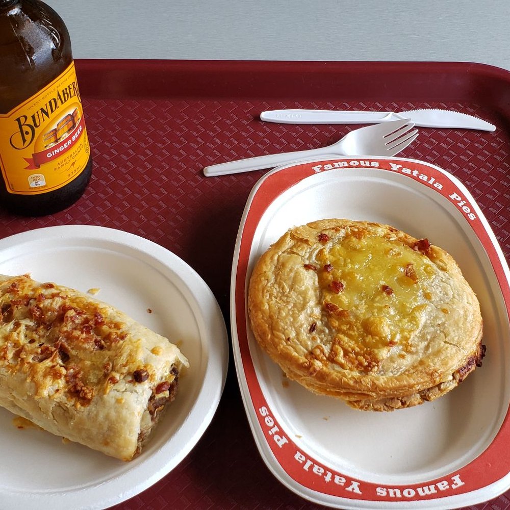 Bacon, cheese, sausage roll on the left, and a steak, bacon, cheese pie on the right, with a ginger beer.