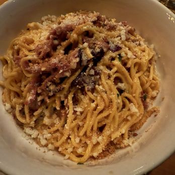 Prato - A white bowl contains a serving of pasta topped with grated cheese, small pieces of meat, and herbs. The dish appears to be served in a restaurant, with a wooden table surface visible and a small bowl in the background. - Pizza Near Me - Winter Park, Florida