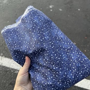 Michaels - 3 folded yards of "Navy Swirling Stars" cotton fabric, being held by a hand in a parking lot - Arts & Crafts Near Me - Emeryville, California Michaels - 3 folded yards of "Navy Swirling Stars" cotton fabric, being held by a hand in a parking lot - Arts & Crafts Near Me - Emeryville, California
