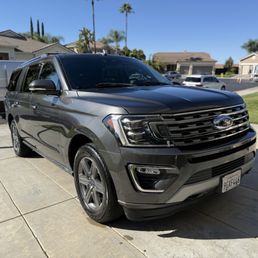 A black Ford SUV is parked on a concrete driveway in a residential area with houses, trees, and other vehicles visible in the background.