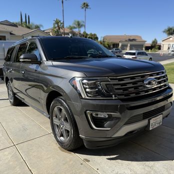 Caleb’s Auto Detailing - A black Ford SUV is parked on a concrete driveway in a residential area with houses, trees, and other vehicles visible in the background. - Auto Detailing Near Me - Riverside, California