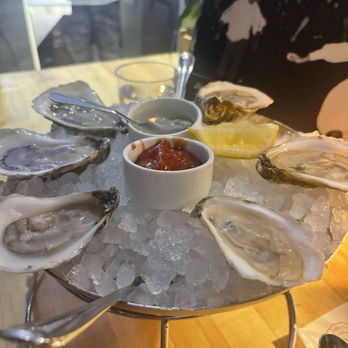 The Longfellow Bar - Oysters - A platter of fresh oysters on ice with lemon wedges and two dipping sauces, likely at a seafood restaurant. - New American Near Me - Cambridge, Massachusetts