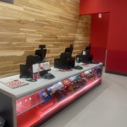 Do they have employees anymore? - Three checkout stations with cash registers and card readers are arranged on a counter in a retail store, with snack items displayed below.