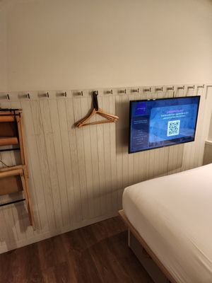 Photo of Moxy NYC Times Square - New York, NY, US. The wall opposite the bed with the series of hooks, adjustable TV screen and fold out seating.