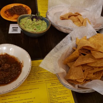 Amuleto Mexican Table - Guacamole, salsa, and chips - A restaurant table features a bowl of guacamole, a basket of tortilla chips, and a small dish of salsa, with drinks and a menu nearby. - Mexican Near Me - Waltham, Massachusetts