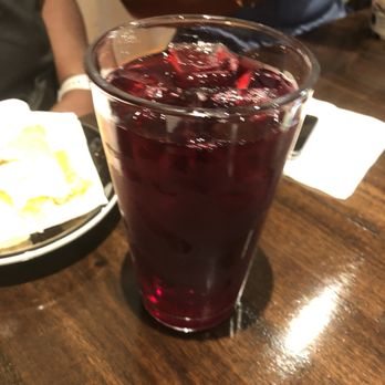 Sankofa Cafe - Hibiscus tea - A tall glass filled with dark red hibiscus tea and ice cubes is placed on a wooden table in a restaurant setting. - Coffee & Tea Near Me - Montclair, New Jersey