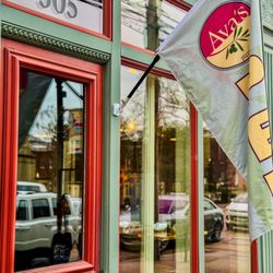 Ava's Pizzeria & Wine Bar - Cambridge - The red-trimmed front door and large street-facing windows of Ava's Cambridge, with the restaurant's flag mounted above the entrance.