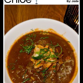 Chloe - Full review on my Instagram (@_edaj_) and TikTok (@_edaj_jade_) - A bowl of soup with herbs and vegetables on top, placed on a wooden table, with part of a black utensil holder visible. - New American Near Me - Washington, DC, District of Columbia