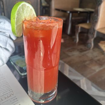 Casa Raya - Michilada - A tall glass of michelada with a lime wedge on the rim, placed on a table in a restaurant with wooden furniture and a menu nearby. - Mexican Near Me - Mount Vernon, Illinois