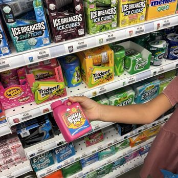 Five Below - Candy - A child extends their arm holding a pink Bubble Buds container in a store aisle stocked with gum and candy products. - Toy Stores Near Me - Jackson Township, New Jersey