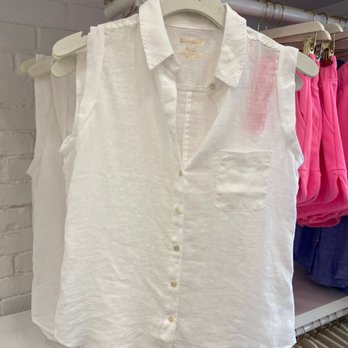 Lilly Pulitzer - A sleeveless white linen shirt with a collar and front pocket is displayed on a hanger in a retail store, with pink clothing visible in the background. - Women's Clothing Near Me - Westerly, Rhode Island