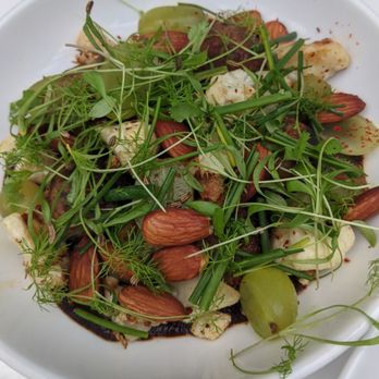 Sava's - A salad featuring mixed greens, almonds, green grapes, and microgreens served on a white plate, with a dark sauce or dressing underneath. - Bars Near Me - Ann Arbor, Michigan