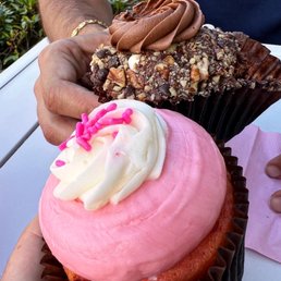 a person holding a cupcake with pink frosting and sprinkles