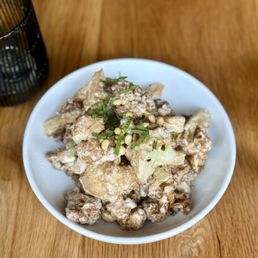 Caramelized Cauliflower - A white bowl contains caramelized cauliflower topped with chopped herbs and pine nuts, placed on a wooden table.