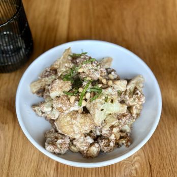 Chloe - Caramelized Cauliflower - A white bowl contains caramelized cauliflower topped with chopped herbs and pine nuts, placed on a wooden table. - New American Near Me - Washington, DC, District of Columbia