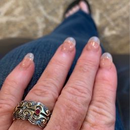 Ring - A close-up of a hand wearing a silver and gold decorative ring with a red gemstone, showing clear, glossy nails, resting on the person's lap.