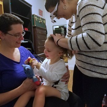 Lice Free Noggins - K is all smiles, sitting comfortably on a parent's lap and playing with a favorite toy while Emma does a very thorough combing. - Lice Services Near Me - Brooklyn, New York
