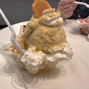 Yeti Eddy - Banana pudding signature shaved ice - A banana pudding signature shaved ice dessert with whipped cream, a cookie, and toppings, served in a clear bowl at a dessert shop. - Candy Stores Near Me - Conroe, Texas