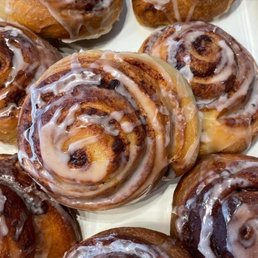 Cinnamon Rolls - A group of cinnamon rolls with icing drizzled on top, placed on a white tray, showcasing their swirled shape and glazed surface.