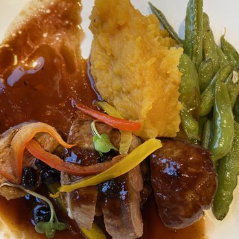 Amaya - Duck breast, butternut squash, sugar snap peas - The image shows a plate of food with mashed sweet potato, green beans, and pieces of meat covered in a dark sauce. The sweet potato is positioned at the top center, while the green beans are on the right side. The meat, with sauce and garnished with small vegetables, is at the bottom of the plate. The dish appears to be a savory meal with a variety of textures and colors. - New American Near Me - Santa Fe, New Mexico