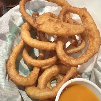 St James Irish Pub - Onions rings were pretty good, I am not a fan of this type of breading on my rings - Fried onion rings served on a paper-lined tray with a cup of dipping sauce, likely at a casual dining or pub setting. - Irish Near Me - Fall River, Massachusetts