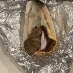 Gyro Pita - A gyro wrap with meat, onions, and sauce partially unwrapped from aluminum foil, showing the ingredients inside.
