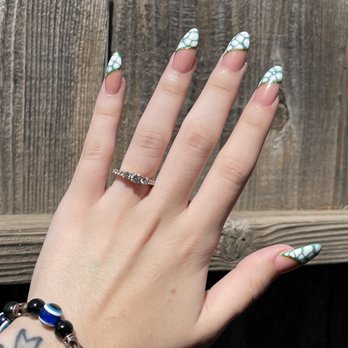 NT Nail Spa - Acrylic fill Gel polish - A hand displays manicured nails with a green and white pattern, wearing a silver ring and a beaded bracelet with blue and black beads, against a wooden fence. - Nail Salons Near Me - Modesto, California
