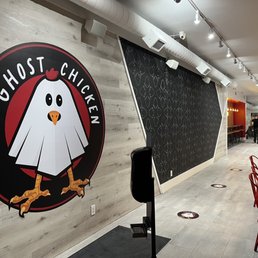 The image shows the interior of Ghost Chicken, a restaurant with a logo of a cartoon chicken on the wall and a seating area with red chairs.