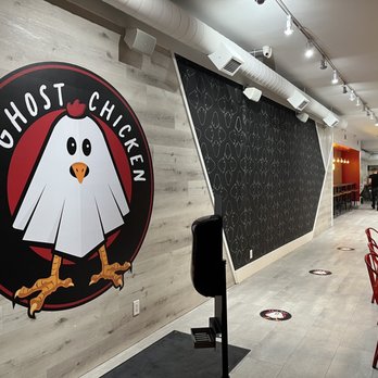 Ghost Chicken - The image shows the interior of Ghost Chicken, a restaurant with a logo of a cartoon chicken on the wall and a seating area with red chairs. - Comfort Food Near Me - Toronto, Ontario