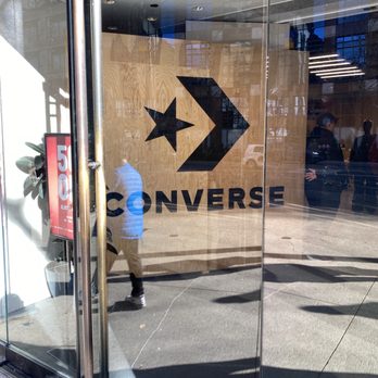 Converse Chicago Popup - Store - Glass storefront with the Converse logo on the interior wall, visible through the glass doors, and a reflection of pedestrians outside. - Shoe Stores Near Me - Chicago, Illinois