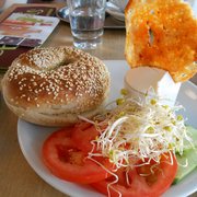 Foto zu Barcomi's - Berlin, Deutschland. Sesambagel mit Philly, Tomaten, Gurke, Kresse und einem mit Chilipaste beträufelten Brotchip