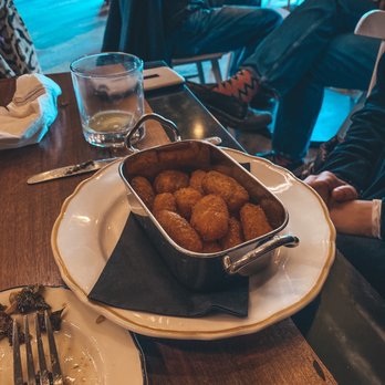 Per Diem - Homemade Tater Tots - A metal basket filled with homemade tater tots sits on a white plate with a black napkin at a restaurant table, with a glass of water and partially eaten food nearby. - American Near Me - Lititz, Pennsylvania