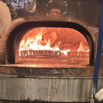 Fat Crow - The wood burning pizza oven - A wood-fired pizza oven with an arched opening, showing bright flames and burning logs inside. The oven is made of metal and stone, and the interior is heated by the fire, which is visible through the opening. The image captures the process of wood-fired pizza preparation, emphasizing the flames and logs used for cooking. - Pizza Near Me - Newfane, Vermont