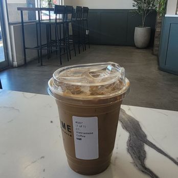 Tea Time - Vietnamese coffee at 30% sweetness...so good! - A plastic cup of Vietnamese iced coffee with a lid and straw is placed on a white marble table inside a cafe with modern decor. - Coffee & Tea Near Me - Albuquerque, New Mexico
