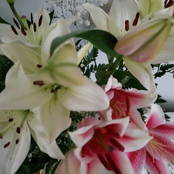 Flower Barn - A close-up image of a bouquet containing white lilies with dark stamens, pink lilies with speckled petals, and green fern-like foliage. The flowers are arranged together, with some blooms partially open and others still in bud form. The background is neutral and out of focus, emphasizing the floral display. - Florists Near Me - Poughkeepsie, New York