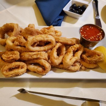 Solar Do Minho - Fried calamari - A plate of fried calamari rings with a side of red dipping sauce and a lemon wedge, presented on a white rectangular dish. - Portuguese Near Me - Belleville, New Jersey