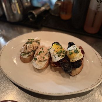 Toro - A white plate holds two types of small appetizers: eggs with herbs on toast and tuna on baguette, garnished with chives. - Tapas Bars Near Me - Boston, Massachusetts