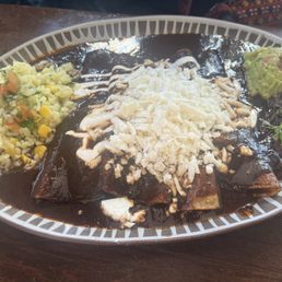 Chilequiles De Mole - A plate of enchiladas de mole topped with cheese and sauce, accompanied by rice, beans, and guacamole, served on a white platter.