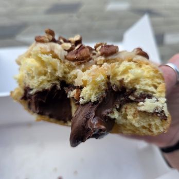 Donerds Donuts - A hand holding a partially eaten donut with chocolate filling and chopped nuts on top, with a white box in the background. - Donuts Near Me - Bethlehem, Pennsylvania